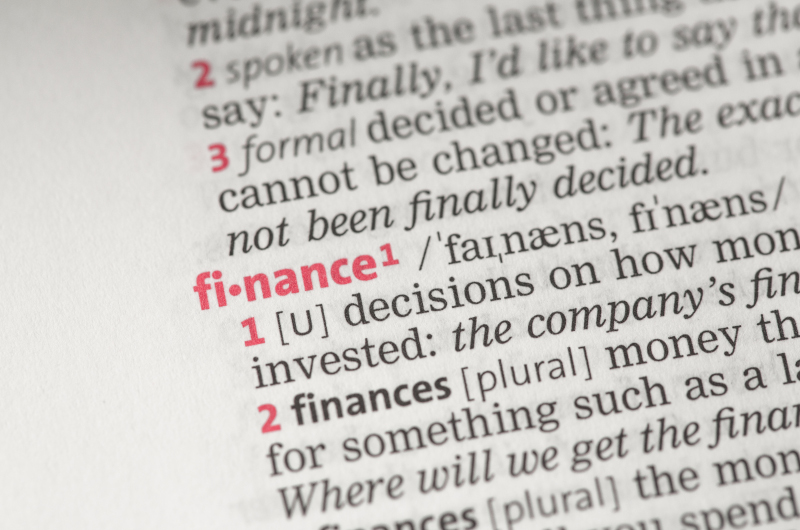 Close-up of a dictionary page showing the word finance in bold red text, with its pronunciation and definition from the financial entry visible.