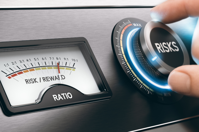 A hand turns a large dial labeled RISKS next to a gauge showing a financial risk/reward ratio, with the needle pointing toward a high risk setting.