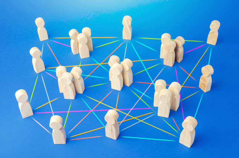 Wooden human figures are arranged in groups on a blue surface, connected by multicolored lines representing an organisation’s network or social connections.